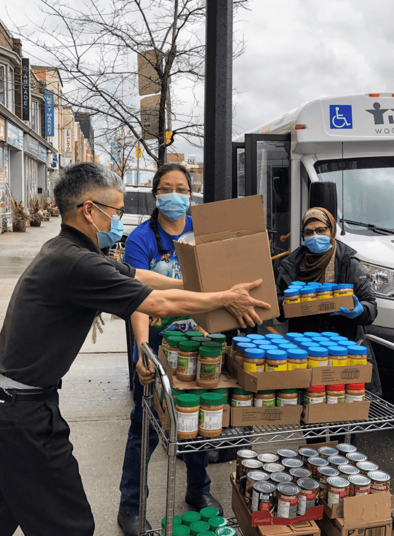 Four people wearing masks on the street loading non-perishable food items into a WoodGreen vehicle
