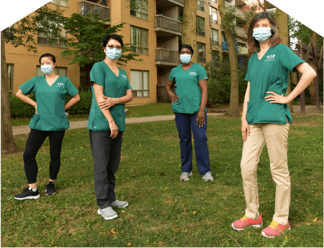 our WoodGreen Personal Support Workers wearing masks and physically distanced from each other, standing outside a building surrounded by trees.