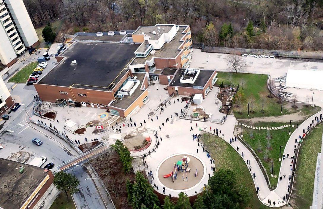Aerial photo of a school yard with a long line of people following a walkway waiting to be vaccinated.
