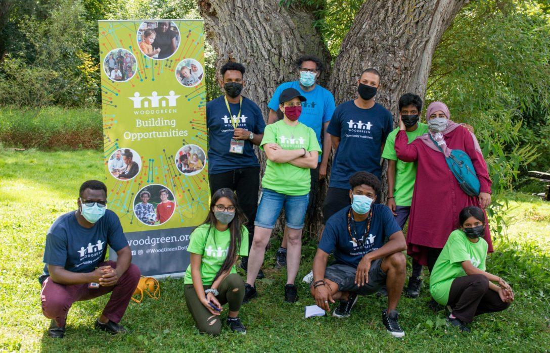 A group of 10 people standing outside in front of a tree, all wearing masks and in different poses.