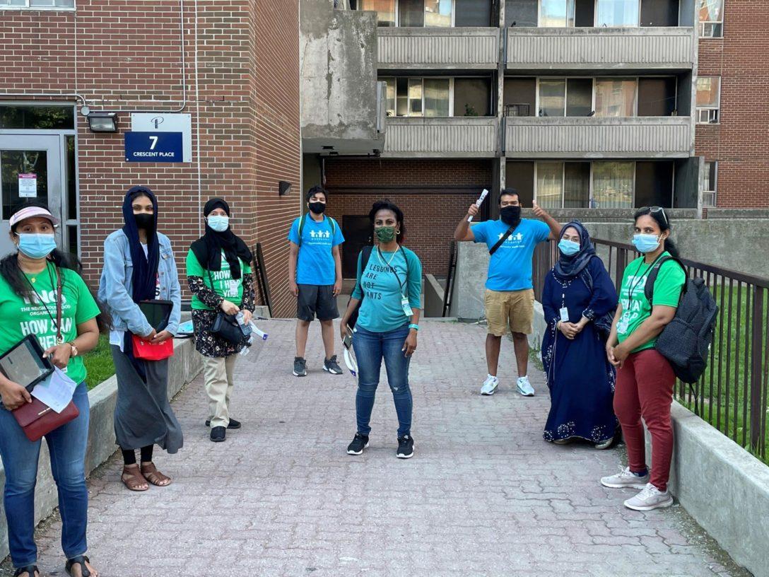 A group of volunteers standing in front of a building, socially distanced and wearing masks.